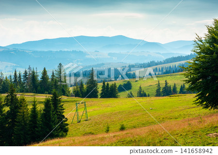 rural scene in carpathian mountain landscape. summer countryside view with rolling hills in lush green grass. forested slopes in the distance rural scene in carpathian mountain landscape. summer countryside view with rolling hills in lush green grass. forested slopes in the distance 141658942