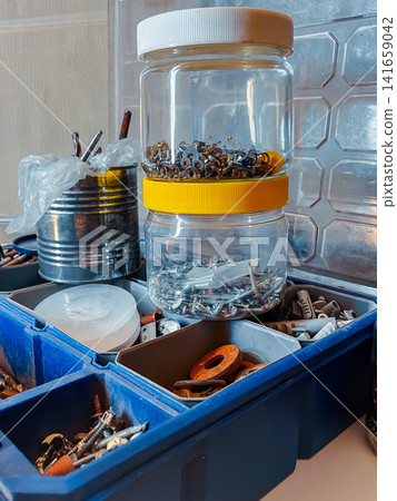 Storing fasteners and assorted small items in clear jars, a tin can, and a compartmentalized toolbox, showing a collection of hardware for repair and maintenance work Storing fasteners and assorted small items in clear jars, a tin can, and a compartmentalized toolbox, showing a collection of hardware for repair and maintenance work 141659042