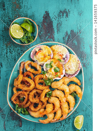 Seafood hot platter baked scallops, fried squid rings and shimps. Top view Seafood hot platter baked scallops, fried squid rings and shimps. Top view 141659375