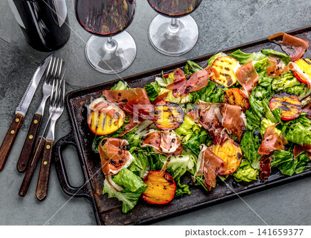 Grilled peach and prosciutto salad with green lettuce, balsamic glaze and wine on dark background Grilled peach and prosciutto salad with green lettuce, balsamic glaze and wine on dark background 141659377