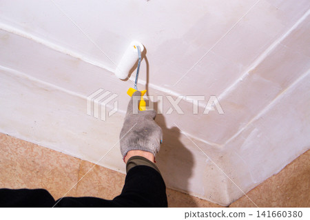 Homeowner painting ceiling with roller. Pleasant changes on budget. DIY cosmetic repair saves money, teaches new skills. Creative handling without hiring professionals Homeowner painting ceiling with roller. Pleasant changes on budget. DIY cosmetic repair saves money, teaches new skills. Creative handling without hiring professionals 141660380