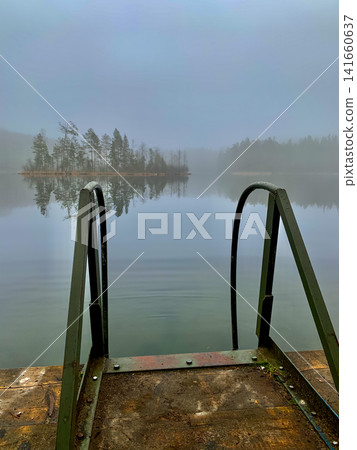 Misty lake with wooden dock and ladder reflecting pine island 141660637