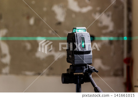 A laser level mounted on a tripod. green lines on a wall. A laser level mounted on a tripod. green lines on a wall. 141661015