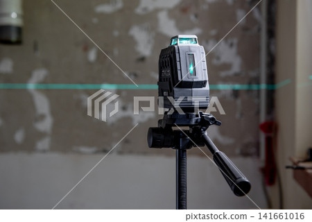 A laser level mounted on a tripod. green lines on a wall. A laser level mounted on a tripod. green lines on a wall. 141661016