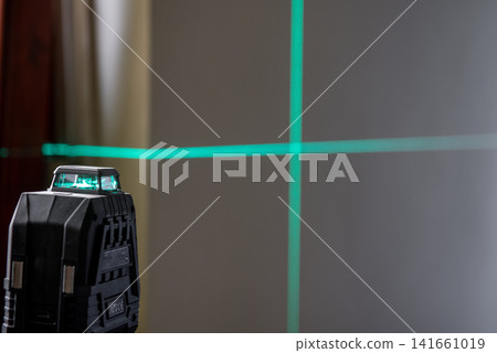 A laser level mounted on a tripod. green lines on a wall. 141661019