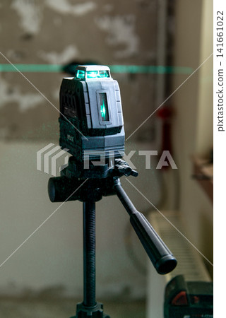 A laser level mounted on a tripod. green lines on a wall. A laser level mounted on a tripod. green lines on a wall. 141661022