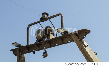 Hydraulic net drum winch and floodlights on fishing boat gantry against clear blue sky Hydraulic net drum winch and floodlights on fishing boat gantry against clear blue sky 141661133