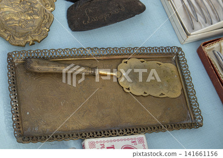 XALO, SPAIN - JUNE 20, 2026.Vintage brass cake server and metallic serving tray on display at a market XALO, SPAIN - JUNE 20, 2026.Vintage brass cake server and metallic serving tray on display at a market 141661156