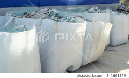 White industrial storage bins filled with green fishing nets at marine harbor on sunny day White industrial storage bins filled with green fishing nets at marine harbor on sunny day 141661159