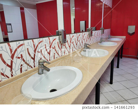 The public toilet has a mirror and white oval sinks for washing hands The public toilet has a mirror and white oval sinks for washing hands 141661293