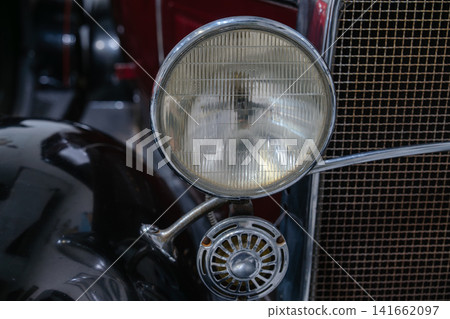 Detailed close up of a vintage headlight and horn mounted on a classic automobile. The image highlights antique automotive craftsmanship and chrome accents. 141662097