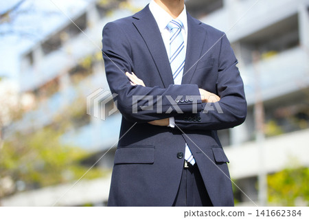 一位二十多歲的商人站在戶外，雙手交叉放在胸前。 141662384