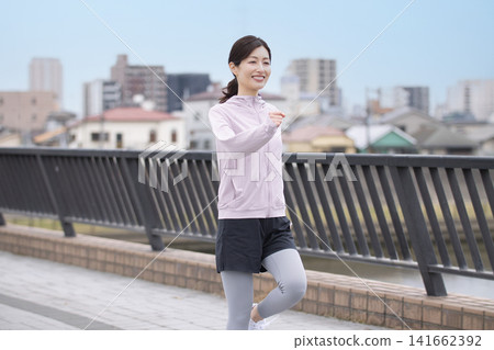 一位中年婦女身穿運動服沿著河岸行走。 141662392