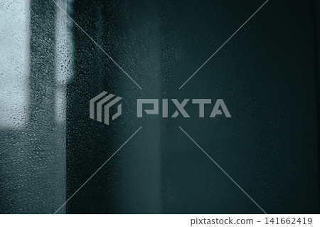 Close-up view of raindrops covering a window pane. Rain drops on a dark glass with blurred urban background. Moody abstract autumnal rainy weather. Close-up view of raindrops covering a window pane. Rain drops on a dark glass with blurred urban background. Moody abstract autumnal rainy weather. 141662419