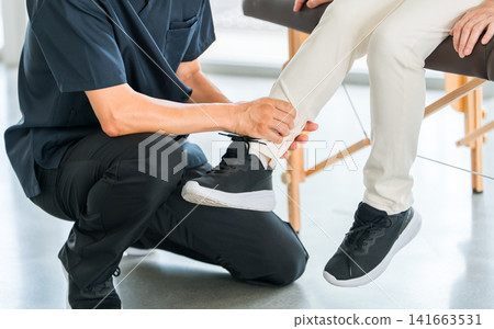 A senior woman receiving rehabilitation treatment for a foot injury at a hospital orthopedics department, along with a doctor and physical therapist. A senior woman receiving rehabilitation treatment for a foot injury at a hospital orthopedics department, along with a doctor and physical therapist. 141663531
