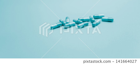 Blue antibiotic capsule pills on pastel blue background. Pharmacy web banner. Antibiotic drug resistance. Antimicrobial capsule pills with space. Health budget and policy. Pharmaceutical industry. 141664027
