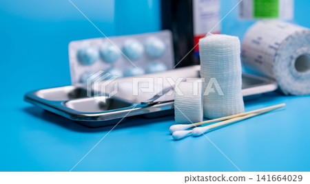 Wound care dressing set. Selective focus cotton stick and elastic cohesive retention bandage on blur stainless steel plate, forceps, conforming bandage, and cotton ball with alcohol. Medical supply. Wound care dressing set. Selective focus cotton stick and elastic cohesive retention bandage on blur stainless steel plate, forceps, conforming bandage, and cotton ball with alcohol. Medical supply. 141664029