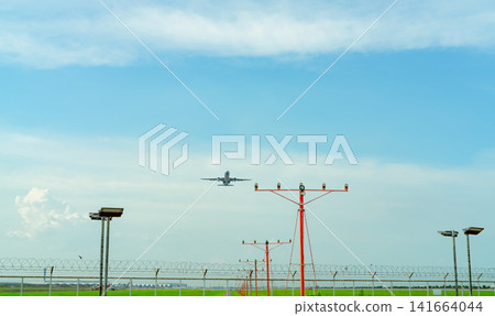 Commercial airplane flying above approach light at the airport. Approach light system concept. Airport runway approach lights. ALS of the airport. Fence for security. Plane take off from the airport. Commercial airplane flying above approach light at the airport. Approach light system concept. Airport runway approach lights. ALS of the airport. Fence for security. Plane take off from the airport. 141664044