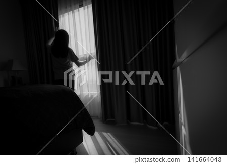 Depressed woman standing by bedroom window. Emotional silhouette reflecting loneliness, anxiety, mental health struggles, isolation, recovery and hope at home. Burnout, mental health awareness. Depressed woman standing by bedroom window. Emotional silhouette reflecting loneliness, anxiety, mental health struggles, isolation, recovery and hope at home. Burnout, mental health awareness. 141664048