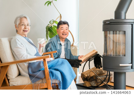 A senior couple chatting happily in the living room of their home, which has a wood-burning stove. A senior couple chatting happily in the living room of their home, which has a wood-burning stove. 141664063