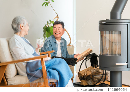 A senior couple chatting happily in the living room of their home, which has a wood-burning stove. A senior couple chatting happily in the living room of their home, which has a wood-burning stove. 141664064