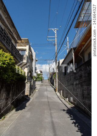 A straight back alley in a sunny city, with the shadows of utility poles and houses cast across the road. A straight back alley in a sunny city, with the shadows of utility poles and houses cast across the road. 141664327