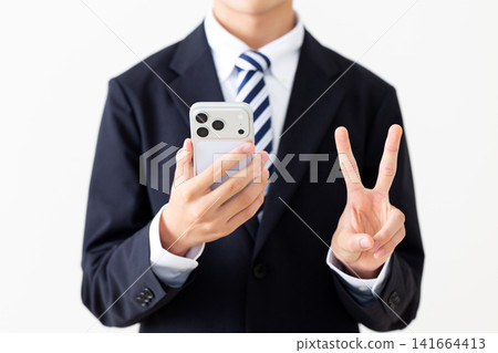 一位身穿西裝的年輕商人手持智慧型手機,比出和平手勢。 一位身穿西裝的年輕商人手持智慧型手機,比出和平手勢。 141664413
