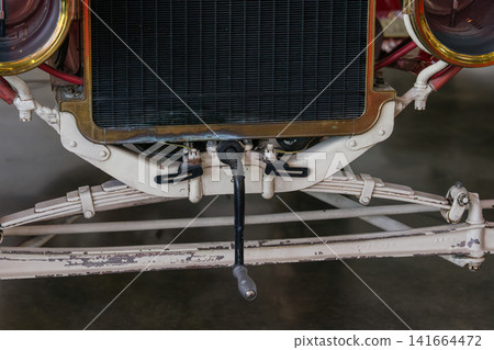 Close up of a vintage car front axle, steering rod, and suspension system beneath the radiator grille. The image highlights mechanical engineering details, worn paint, and historic automotive 141664472