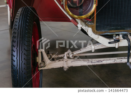 Close up of antique car front suspension and wheel showing detailed linkage and metal framework. The image emphasizes historic automotive design with aged paint and classic engineering elements. Close up of antique car front suspension and wheel showing detailed linkage and metal framework. The image emphasizes historic automotive design with aged paint and classic engineering elements. 141664473