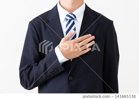 A young businessman in a suit places his hand on his chest. A young businessman in a suit places his hand on his chest. 141665138