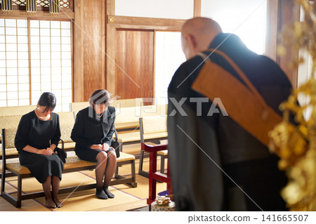 Women in mourning attire bow deeply before a Buddhist monk. 141665507