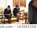 Women in mourning attire bow deeply before a Buddhist monk. Women in mourning attire bow deeply before a Buddhist monk. 141665508