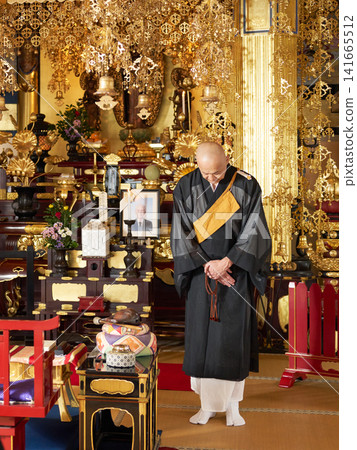 The head priest bows before the altar adorned with the portrait and urn of the deceased. The head priest bows before the altar adorned with the portrait and urn of the deceased. 141665512