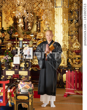The head priest clasps his hands together in prayer at the altar adorned with a portrait of the deceased and an urn. The head priest clasps his hands together in prayer at the altar adorned with a portrait of the deceased and an urn. 141665513