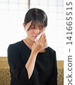 A young woman in mourning clothes wipes away tears with a handkerchief. A young woman in mourning clothes wipes away tears with a handkerchief. 141665515