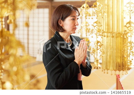 A woman in mourning attire offers prayers at a memorial service. A woman in mourning attire offers prayers at a memorial service. 141665519