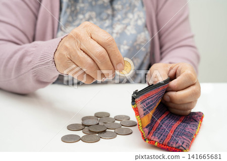 Asian senior or elderly old lady woman holding counting coin money in bag. Poverty, saving problem in retirement. Asian senior or elderly old lady woman holding counting coin money in bag. Poverty, saving problem in retirement. 141665681