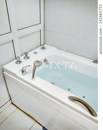 Modern white bathtub with water and chrome fixtures in a clean bathroom setting Modern white bathtub with water and chrome fixtures in a clean bathroom setting 141665753
