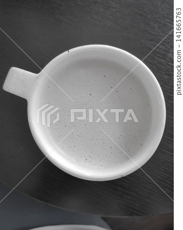 White ceramic coffee cup filled with light-colored beverage on dark wooden table surface White ceramic coffee cup filled with light-colored beverage on dark wooden table surface 141665763
