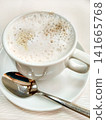 Close-up of cappuccino in white cup with foam and spoon on saucer, elegant table setting 141665768