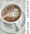 Close-up of coffee cup with frothy surface and bubbles on white saucer, soft background 141665769