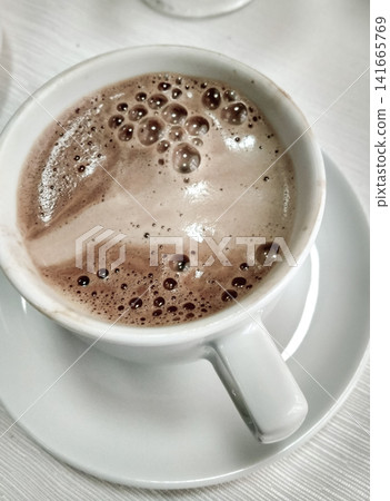 Close-up of coffee cup with frothy surface and bubbles on white saucer, soft background Close-up of coffee cup with frothy surface and bubbles on white saucer, soft background 141665769