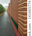 Red brick wall with green ledge along sidewalk in urban area surrounded by trees 141665774