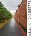 Tree-lined pathway beside brick wall leading to residential buildings under cloudy sky 141665775