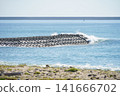 The waves of the sea crash against the breakwater's wave-dissipating blocks, creating a white splash. 141666702