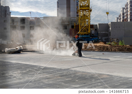 Construction worker in orange helmet cutting concrete slab with dust cloud 141666715