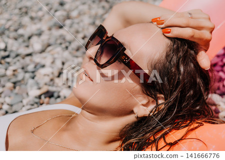 Woman beach sunglasses young lady lying on pebbly shore enjoying summer vacation sunbathing with wet hair during holiday relaxation 141666776