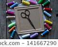 Vintage scissors on blank wooden frame surrounded by colorful sewing threads flat lay craft background with copy space for text or mockup design 141667290
