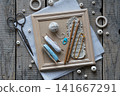 Rustic handmade craft flat lay with wooden crochet hooks decorative cords tassels wooden beads scissors and textile accessories arranged on wooden frame background top view 141667291