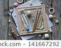 Creative handmade textile flat lay with blue decorative cord wooden crochet hooks tassels wooden beads scissors and craft accessories arranged on rustic wooden frame background 141667292